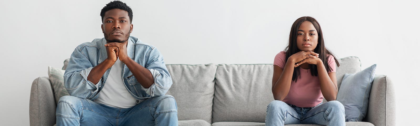 A couple sit on opposite sides of the couch showing no interest in one another.