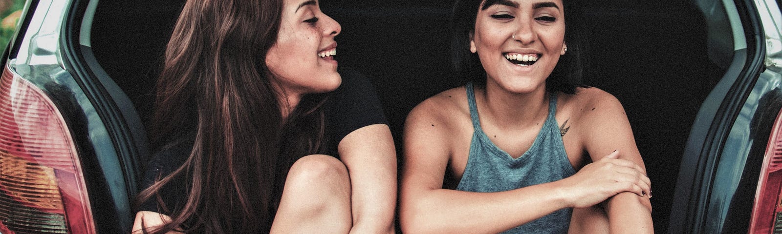 two smiling girls with brown hair sitting in open back of car