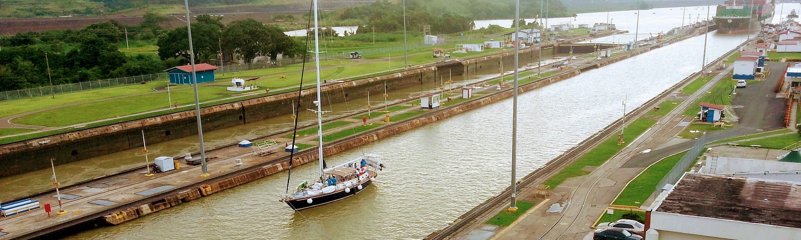 Photo showing a small yacht and a large ship entering the Miraflores Locks, Panama Canal