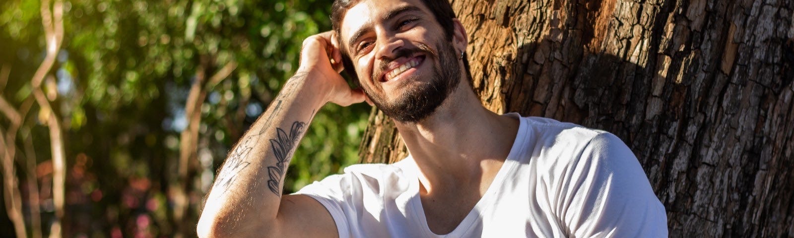 Smiling young man with a tattoed forearm sitting in the sun