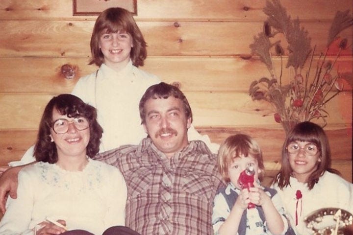 Family photo in 1979. Mom dad and three kids sitting on a couch against a wood panelled wall.