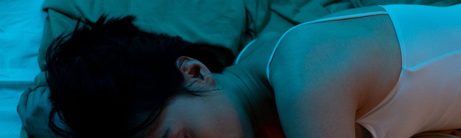 Young, malaised woman lying down in the dark on a bed.