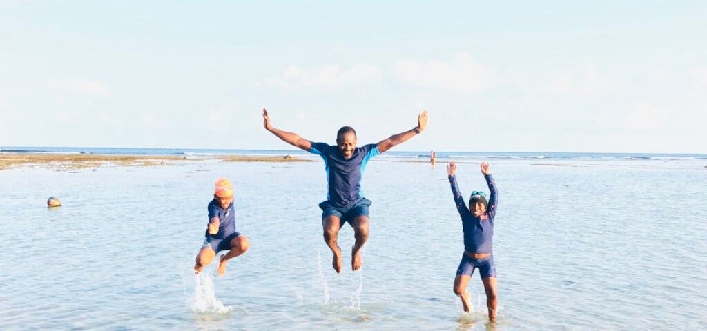 A man and two kids jumping happily up in their beach clothes