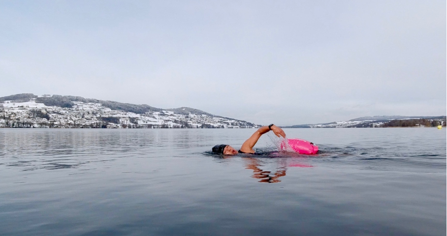 Female swimming front crawl in lake with snow on the surrounding hills.