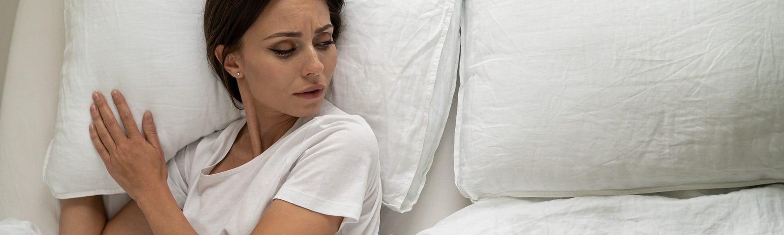 A woman stares sadly at the empty side of her bed.