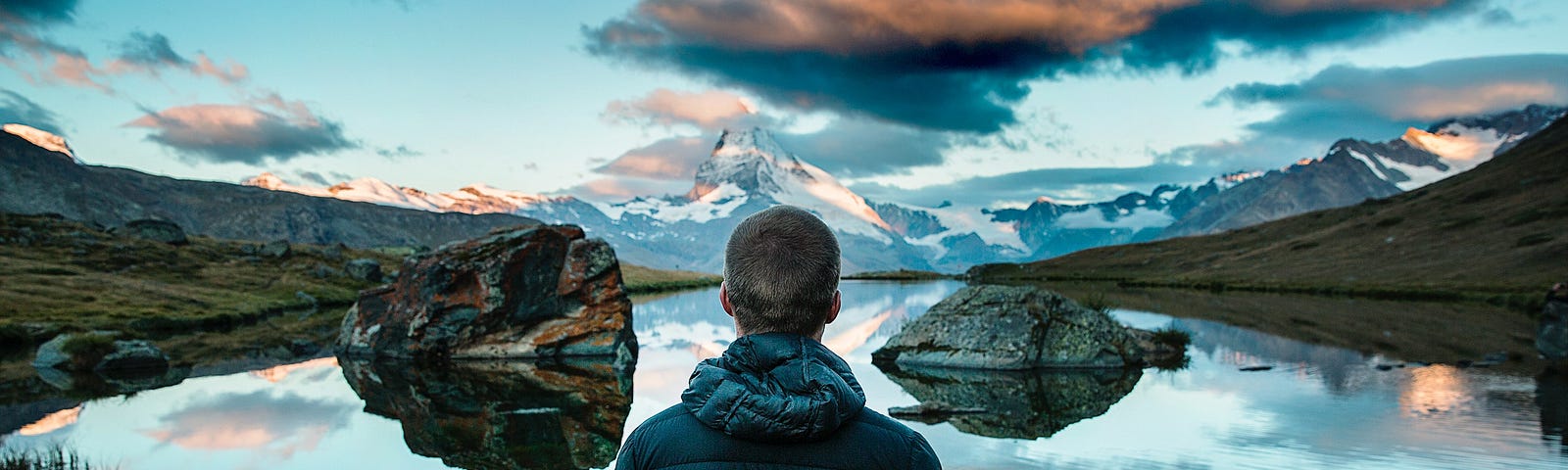 rear view of man looking out over lake with reflection of sky and clouds