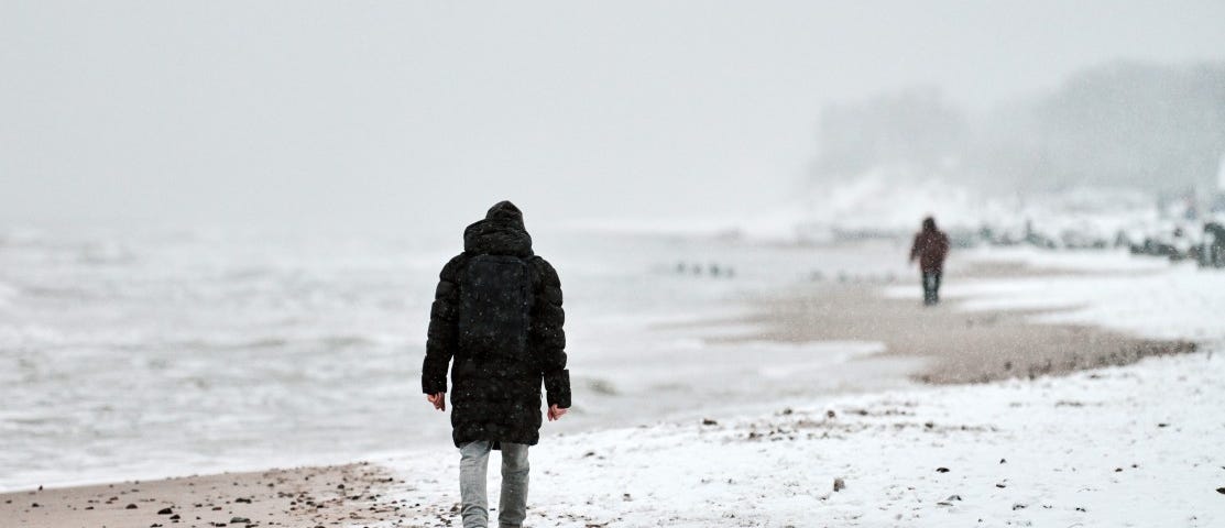 A ma walks sadly down a winter beach by himself.