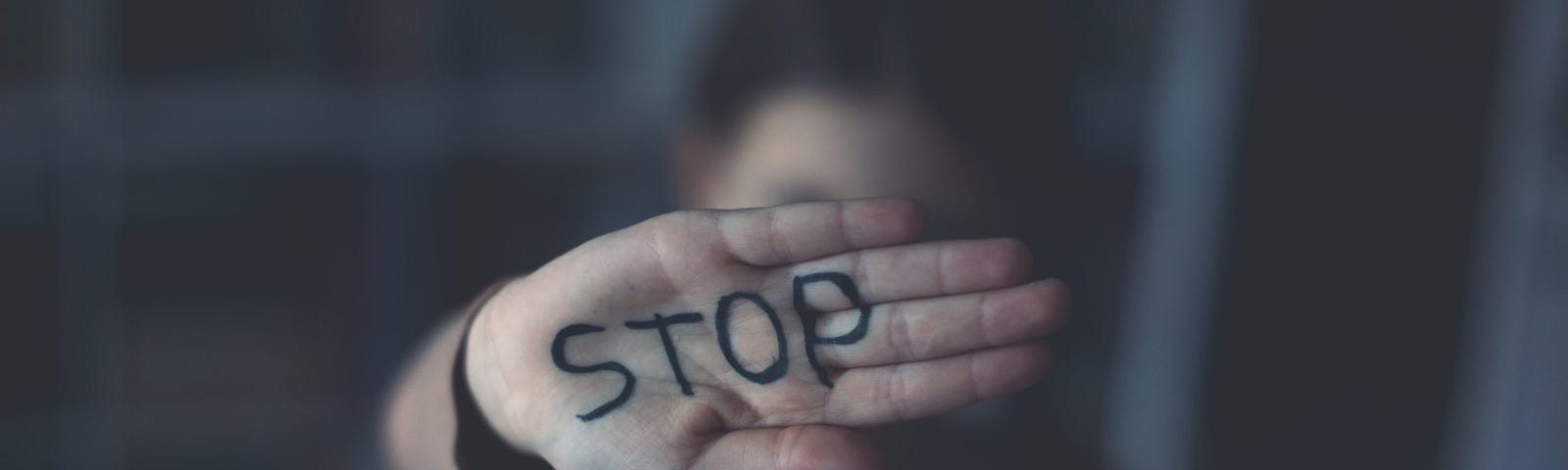 A person’s palm is raised, flat, and bears the word “STOP” in black ink.