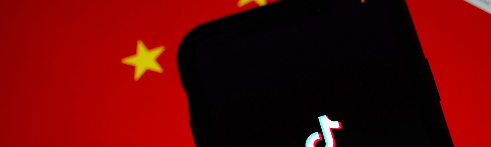 A phone displaying the TikTok logo is placed in front of a Chinese flag.