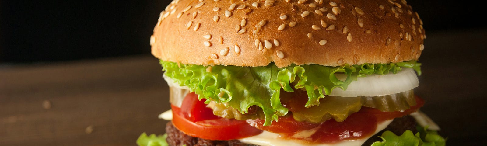 A large hamburger on a wooden table with pepper and sesame.
