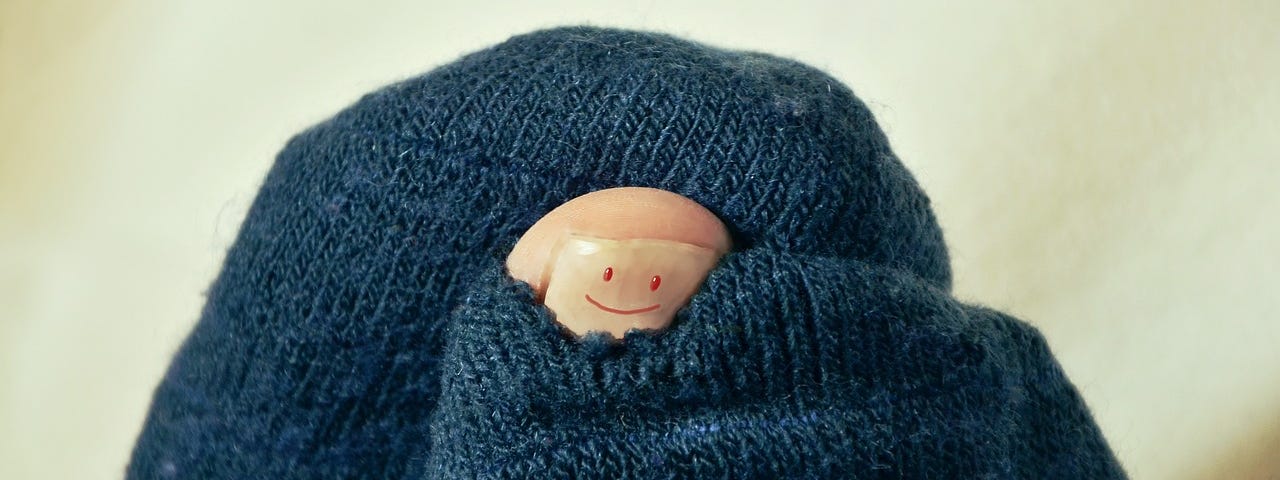 Image of a big toe with a smiley face painted on it, poking out of a hole in a woolen sock