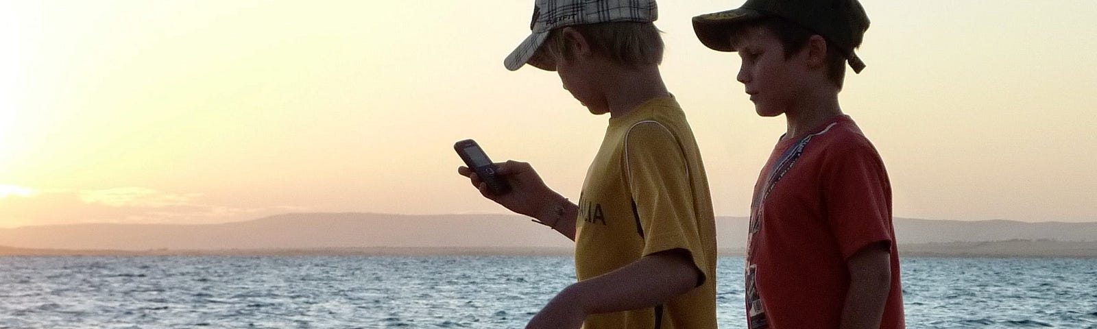 Two boys standing in twilight searching for information on a mobile phone