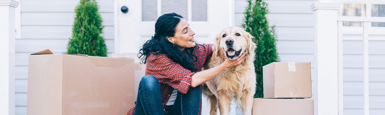 A woman pets a dog while sitting next to moving boxes.