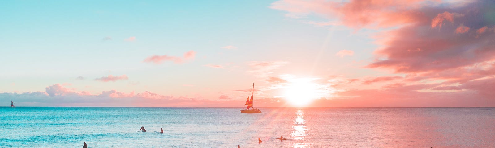 Sunset over a Hawaiian beach with surfers, paddle surfers and a boat.