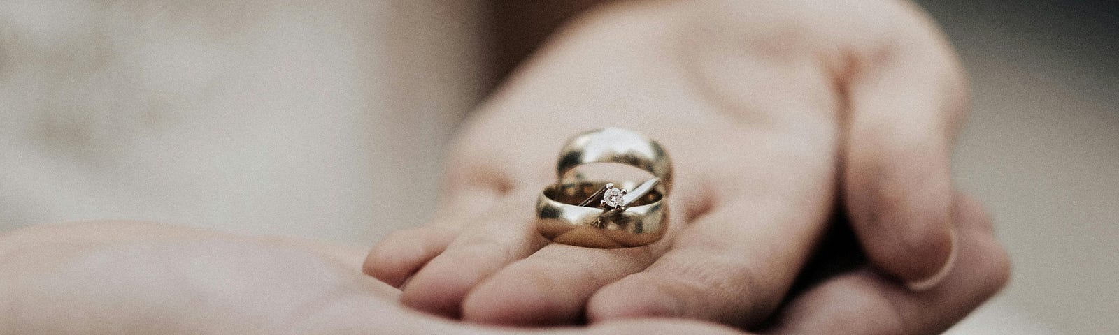 Two palms, one on top of the other with two wedding rings in the top palm