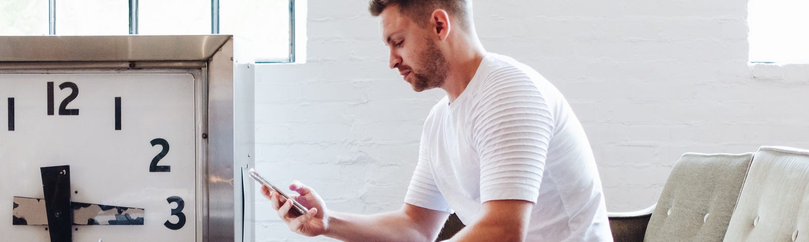 A man sits in front of his laptop, anxiously looking at his phone