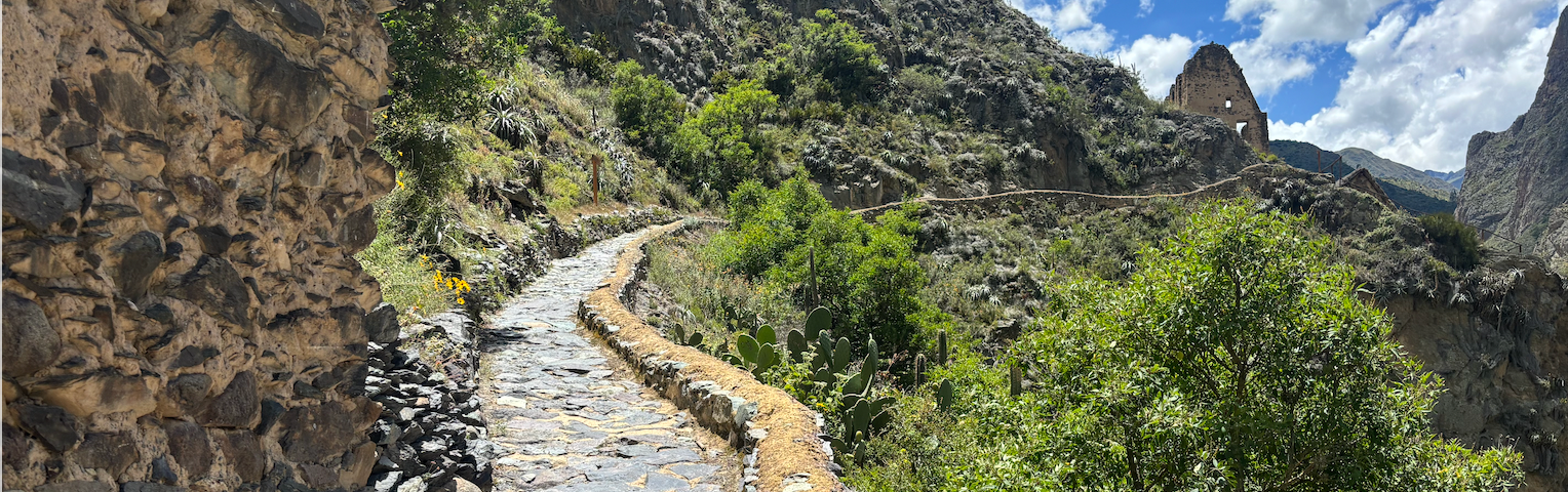 Ancient stone path on the edge of a mountain under blue skies in Peru. It disappears in the distance, looking mysterious and enticing. We want to see where it goes.