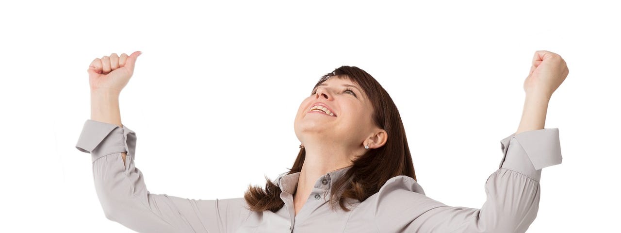 Woman with shoulder length hair and wearing smart blouse has her arms up and open in a gesture of achievement or excitement