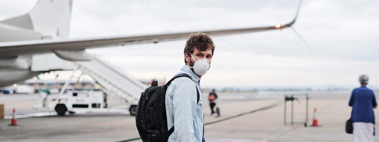 A man wearing a mask about to board a plane.