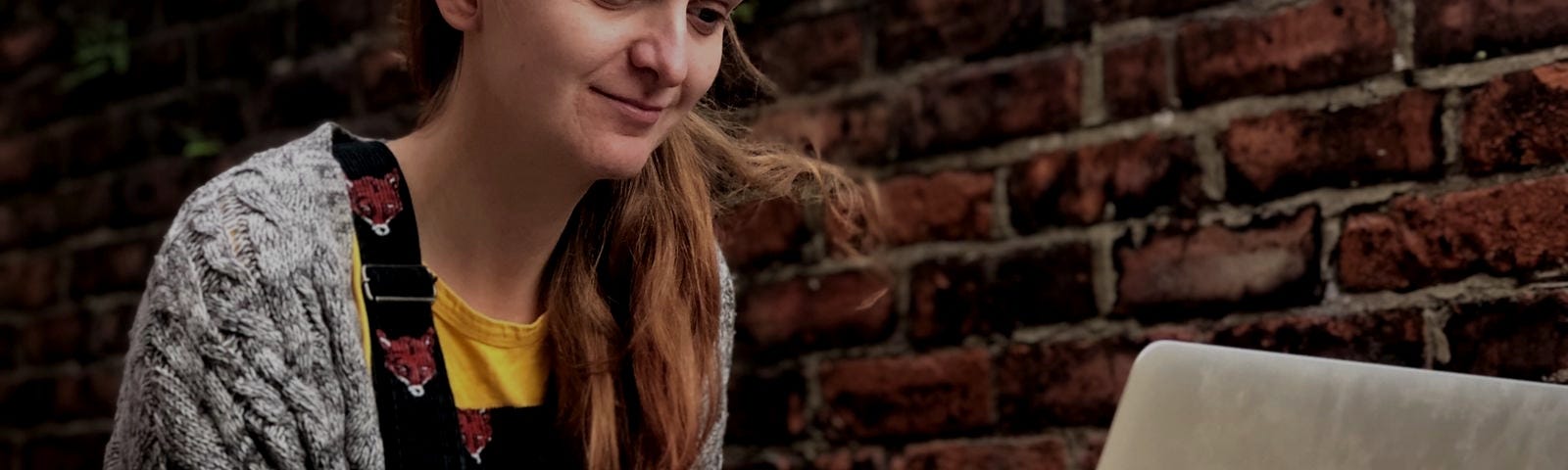 Rachel sits at a table outside. She is typing at her laptop and smiling.