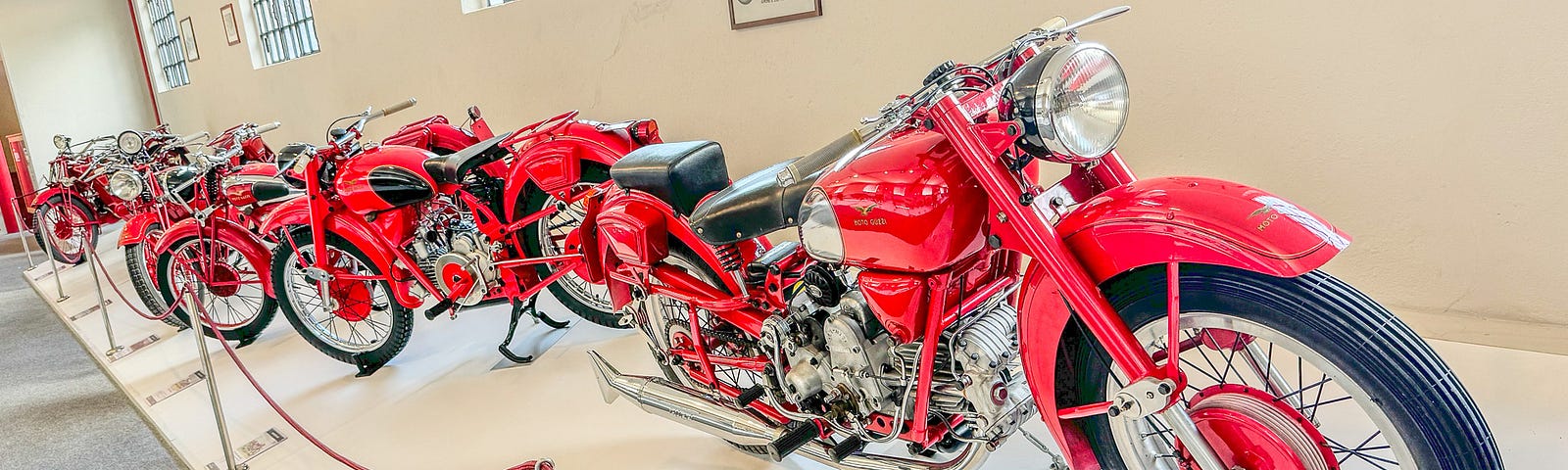 A row of brilliant red shiny motocycles behind ropes in a museum.