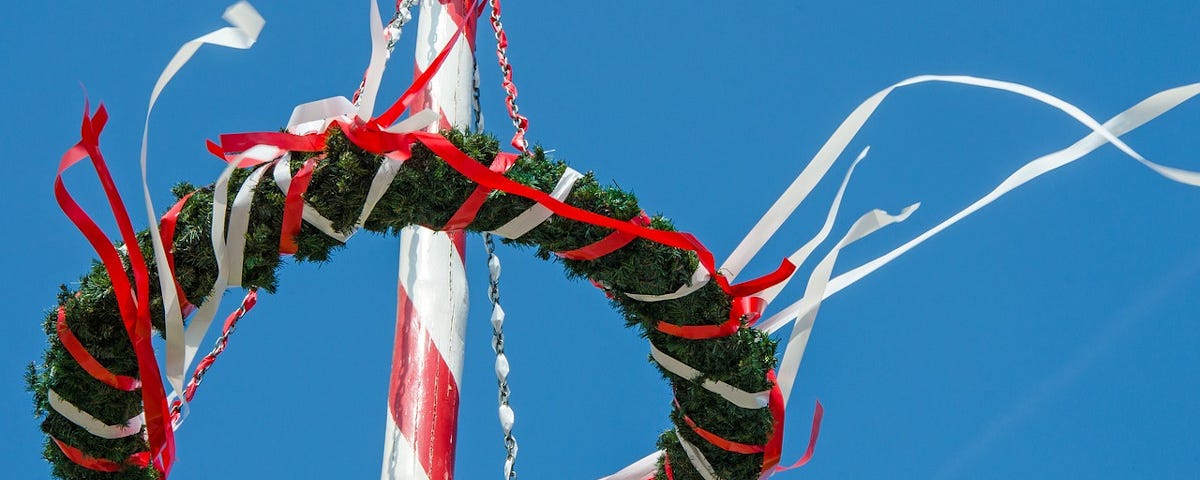 A wreath atop a maypole, with white ribbons streaming from it.