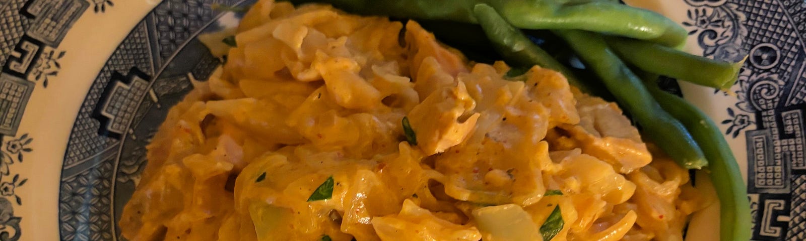 A serving of yellow curry noodles and green beans on a Blue Willow plate.