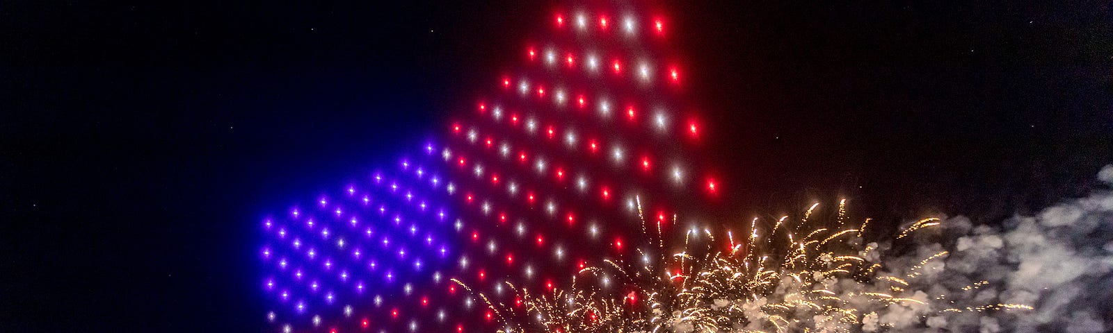 A drones forming the American flag alongside a fireworks display.