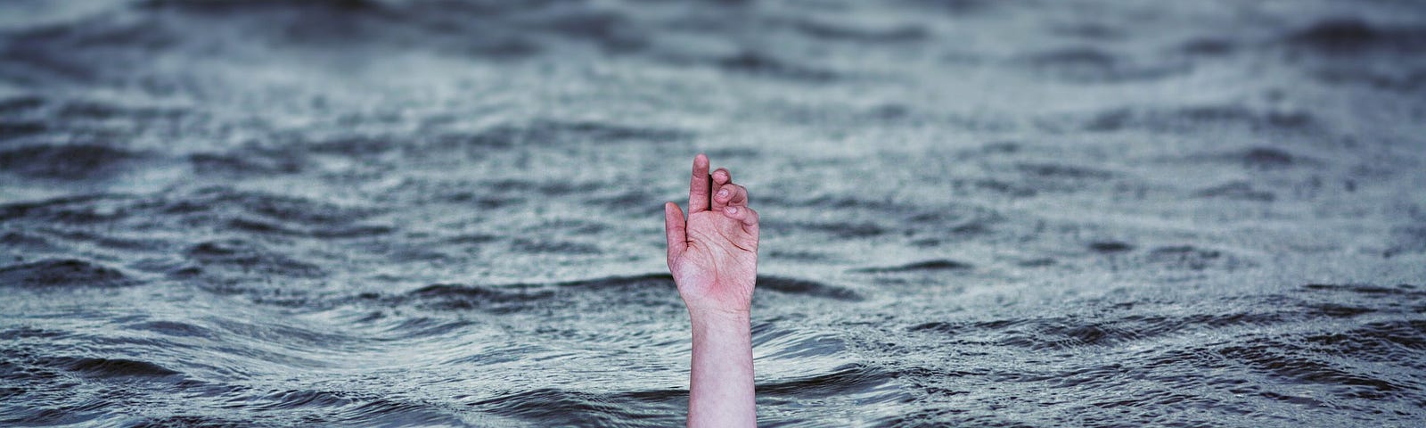 Photo of a hand reaching up out of the blue sea, as if someone is drowning.