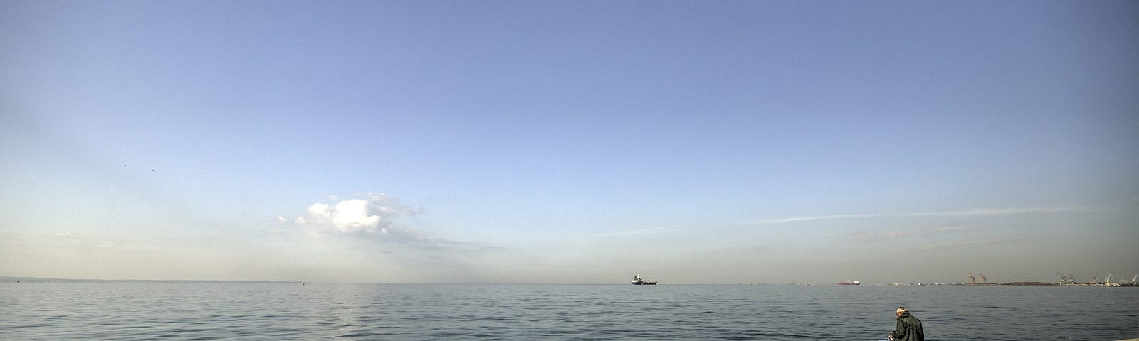 solitary man sitting on long wooden dock fishing