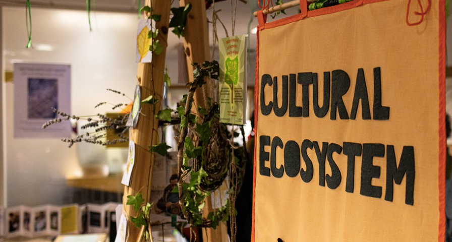 Photo from Cultural Collaborators December Gathering. Showing an organge canvas banner with the writing cultural ecosystem — what if … stiched on in black fabric. Banner created by Time Rebels Ruth and Odette of We Are Makers