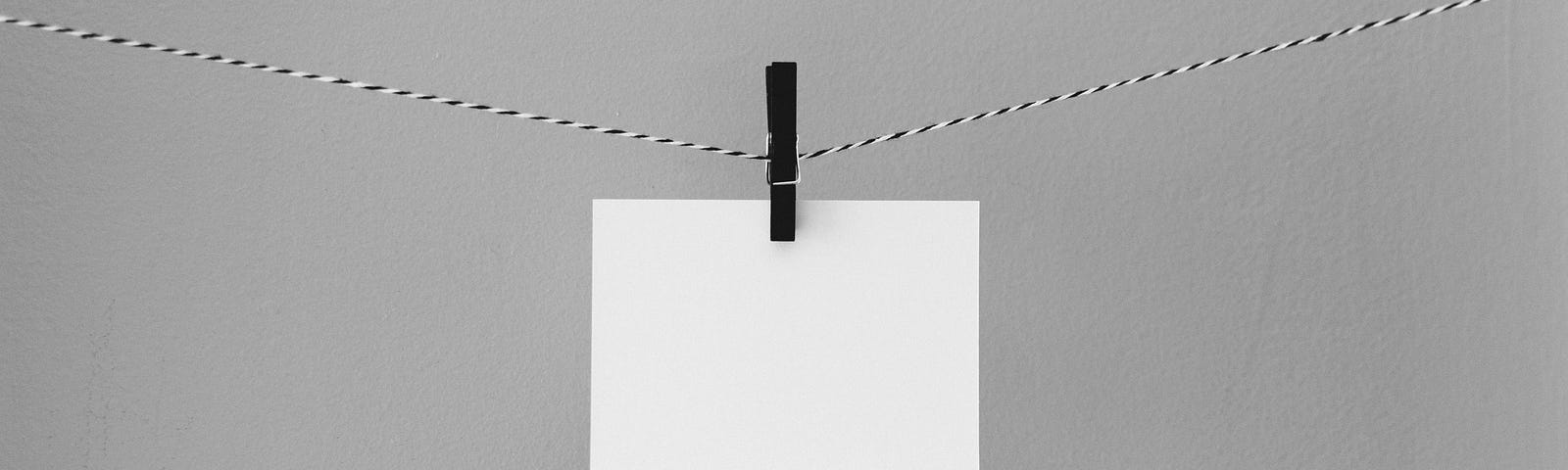 Blank index card on thread, hanging with a clothespin, gray background