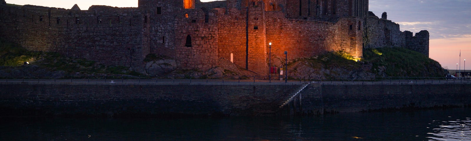 Peel Castle, ancient ruined fortress reflected in water evening light.