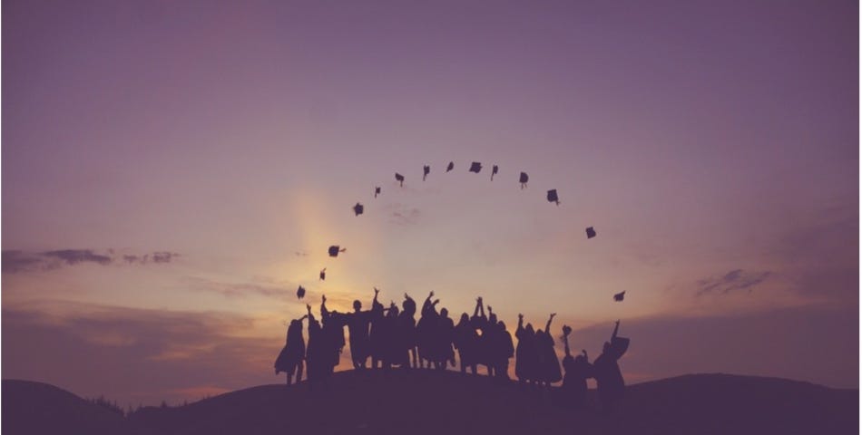 a group of university students celebrating their graduation against the sunset