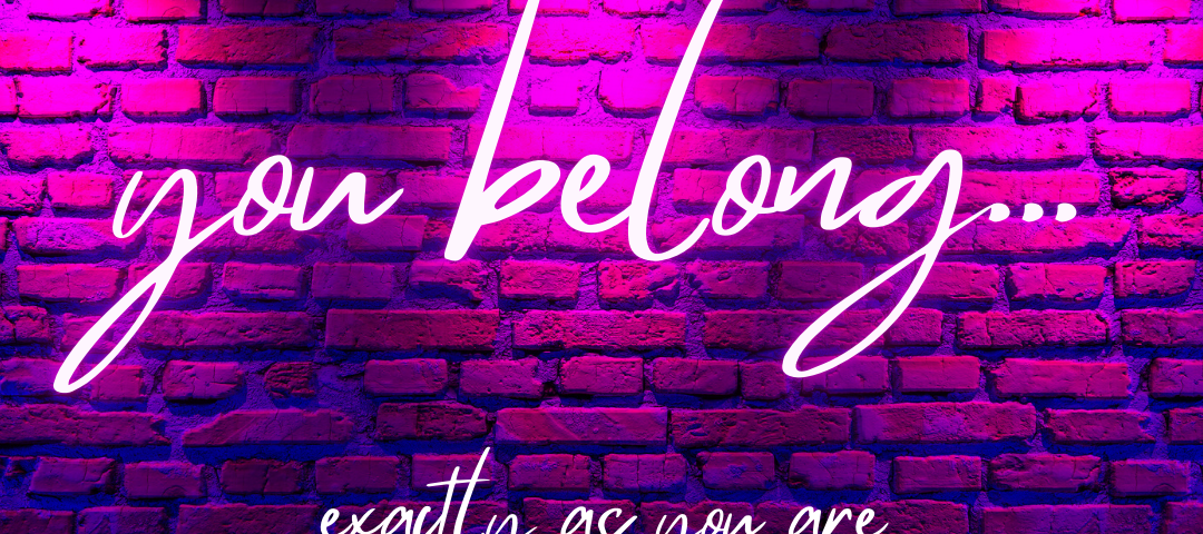 Image of a pink, purple, and blue lit brick wall with neon text reading “you belong… exactly as you are”