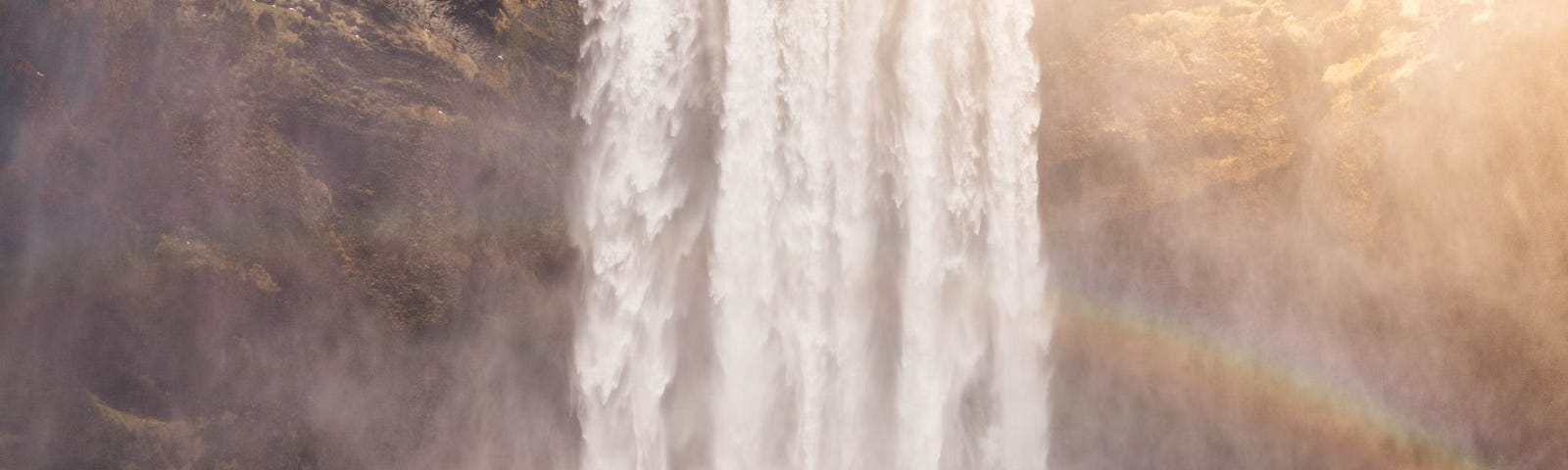 This image features a man standing in a stream with his arms wide open towards a rainbow in the distance