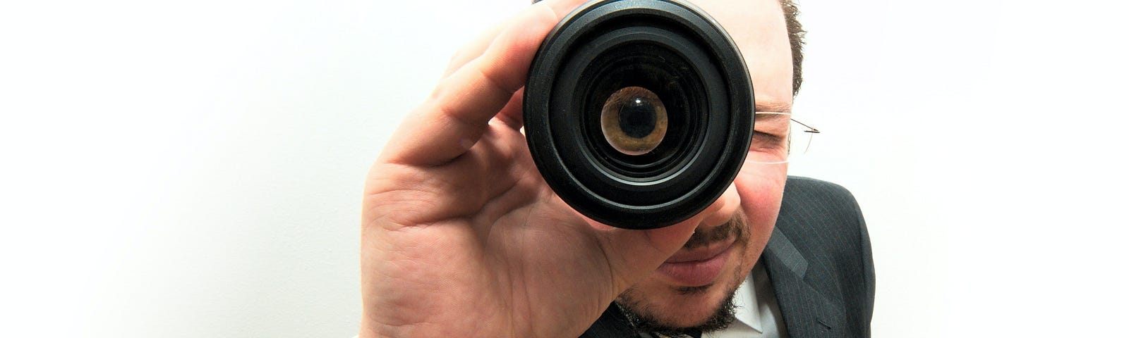 A man in a black suit and tie looking through a monocular.