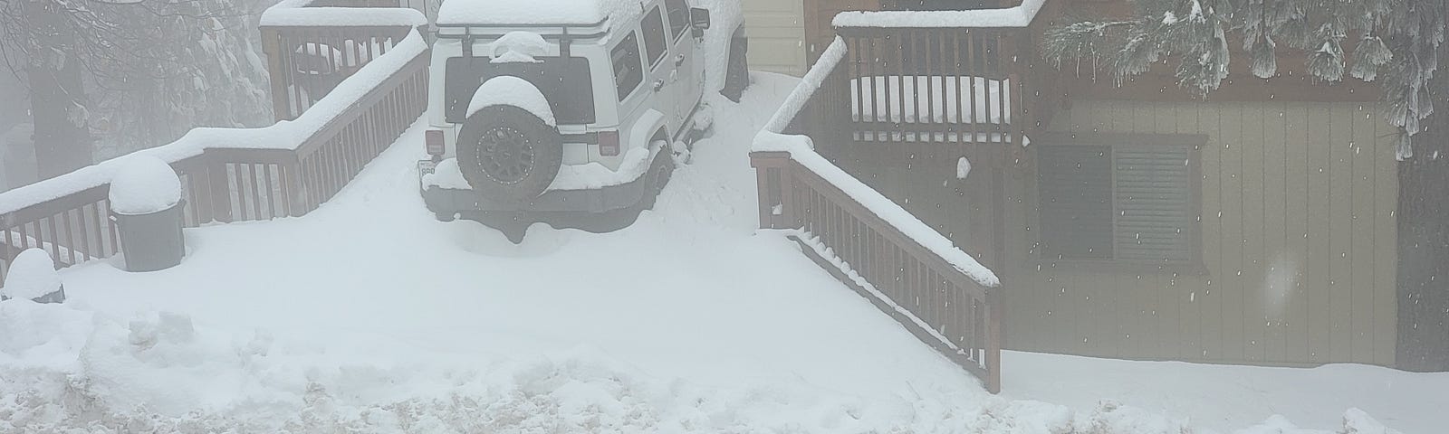 Jeep parked in front of a garage being slowly covered by snow on a cloudy day in the mountains. The street has been freshly plowed, but the Jeep is stuck behind the piles of snow left by the plow.