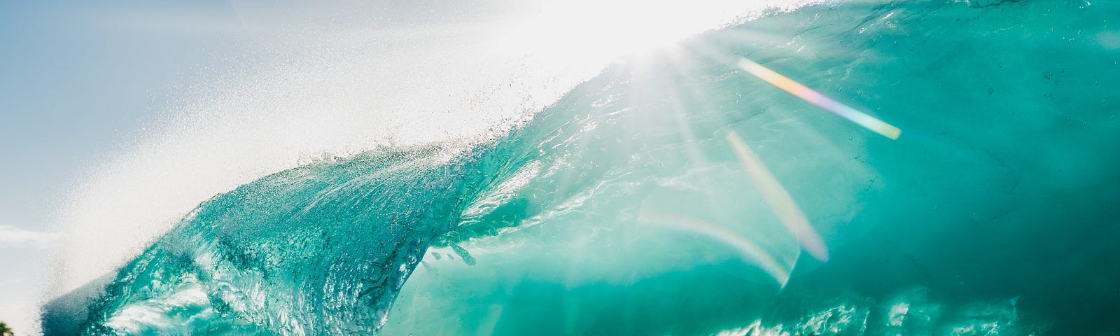 Sunlight sparkling on a turquoise-green ocean wave.