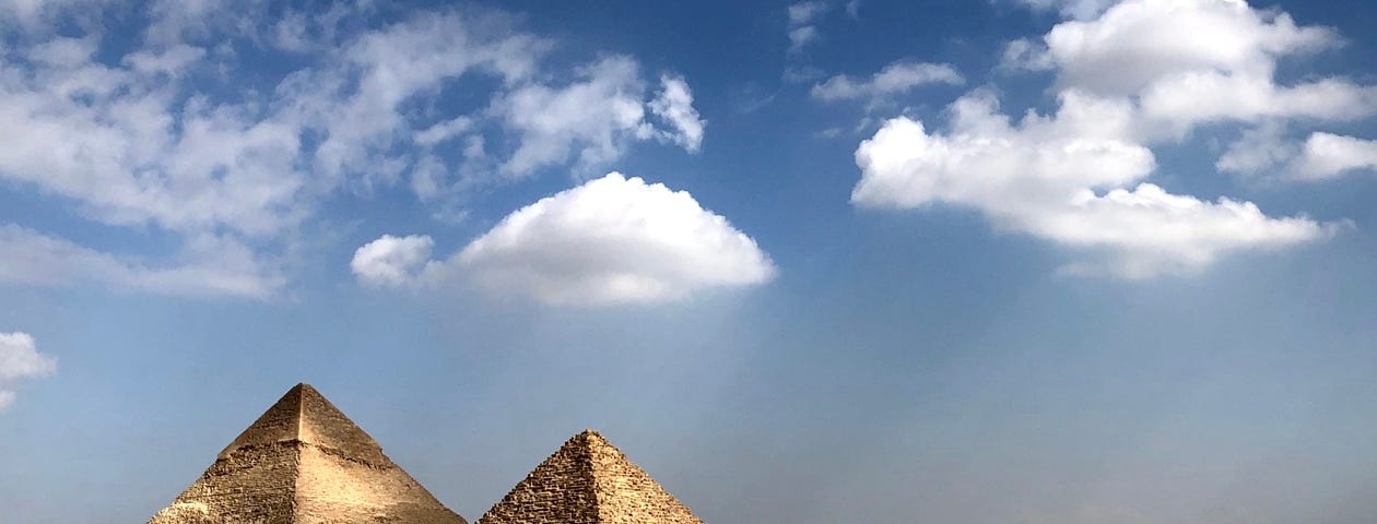 A view of two tall pyramids and three smaller ones under a blue sky with patches of white clouds.