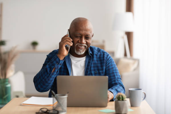 Older man talking on phone while on laptop.