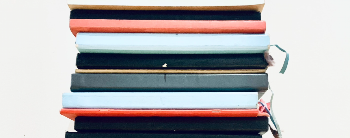 A stack of sketch books piled up in red, black and sky blue