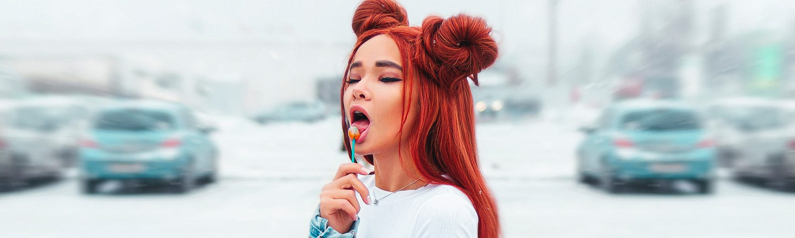 A woman in a denim jacket with red hair licking a lollipop standing in a carpark. Photo: Andrey Zvyagintsev on Unsplash