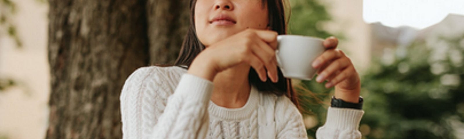 Asian women deep in thought, having coffee alone at outside table.