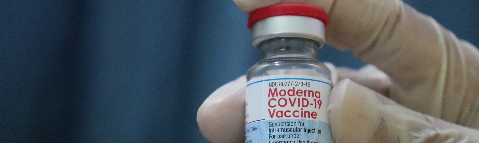 Hand in a surgical glove holding a vial of Moderna COVID-19 vaccine.