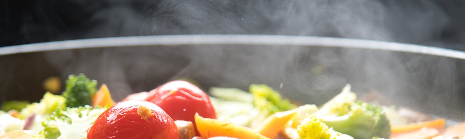 A pot of simmering mix vegetables. bright red tomatoes, broccoli, cauliflowers, carrots and leeks. they look delicious.