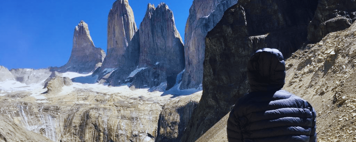 person sitting on a rock in front of mountain peaks and a turquoise lagoon