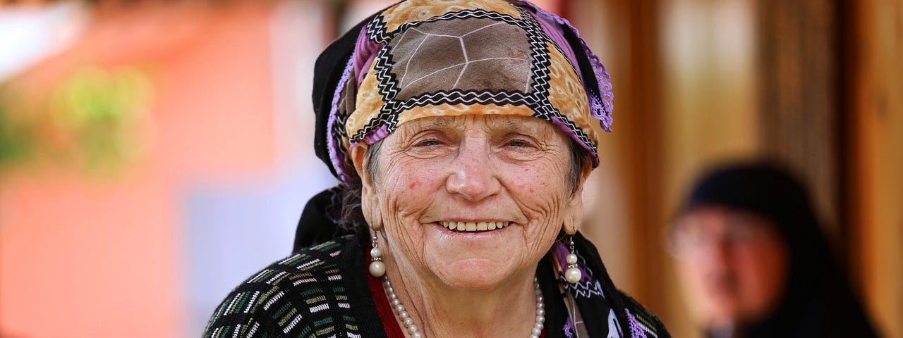 An Eastern European older woman with a head scarf smiles