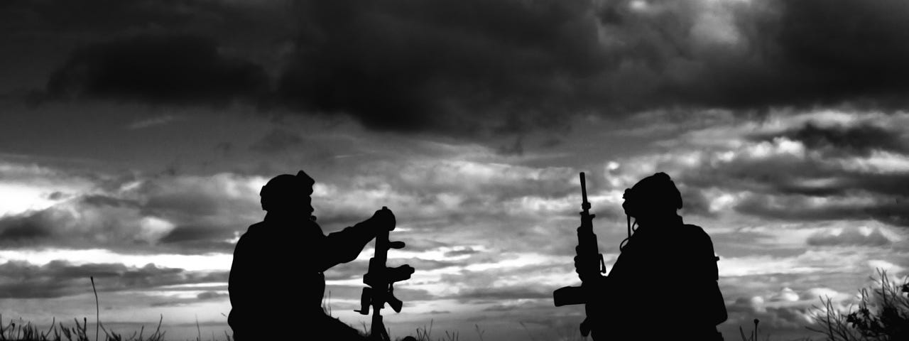 Two soldiers with guns sitting in a black and white photo as silhouettes agains the sunset.