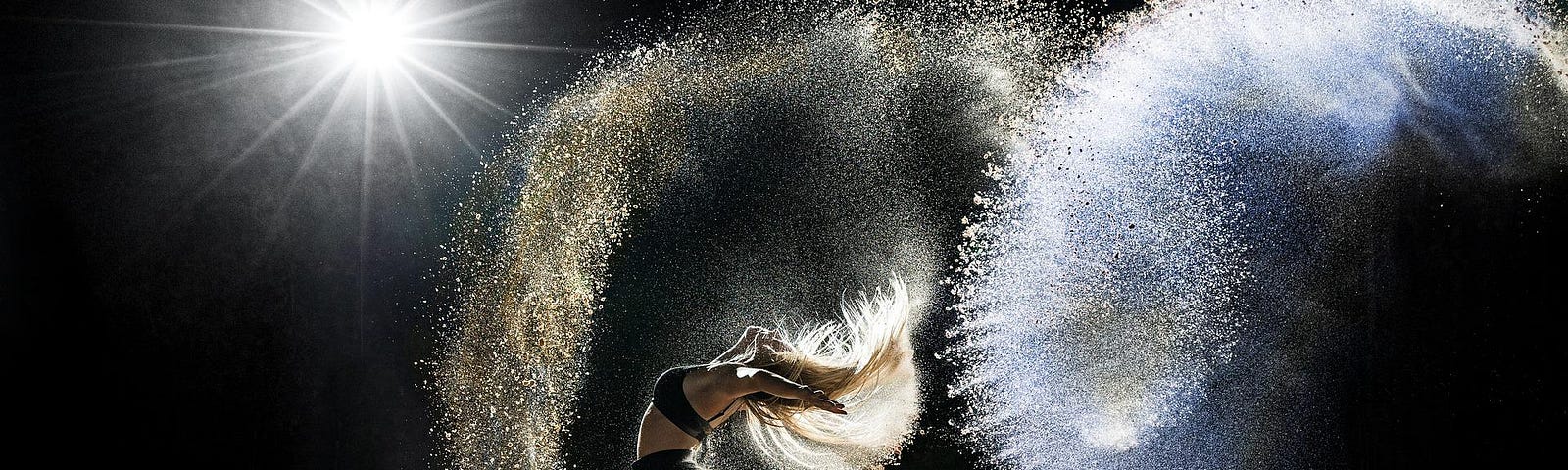 A woman dances on a field of sand, throwing sand into the air to catch the light.